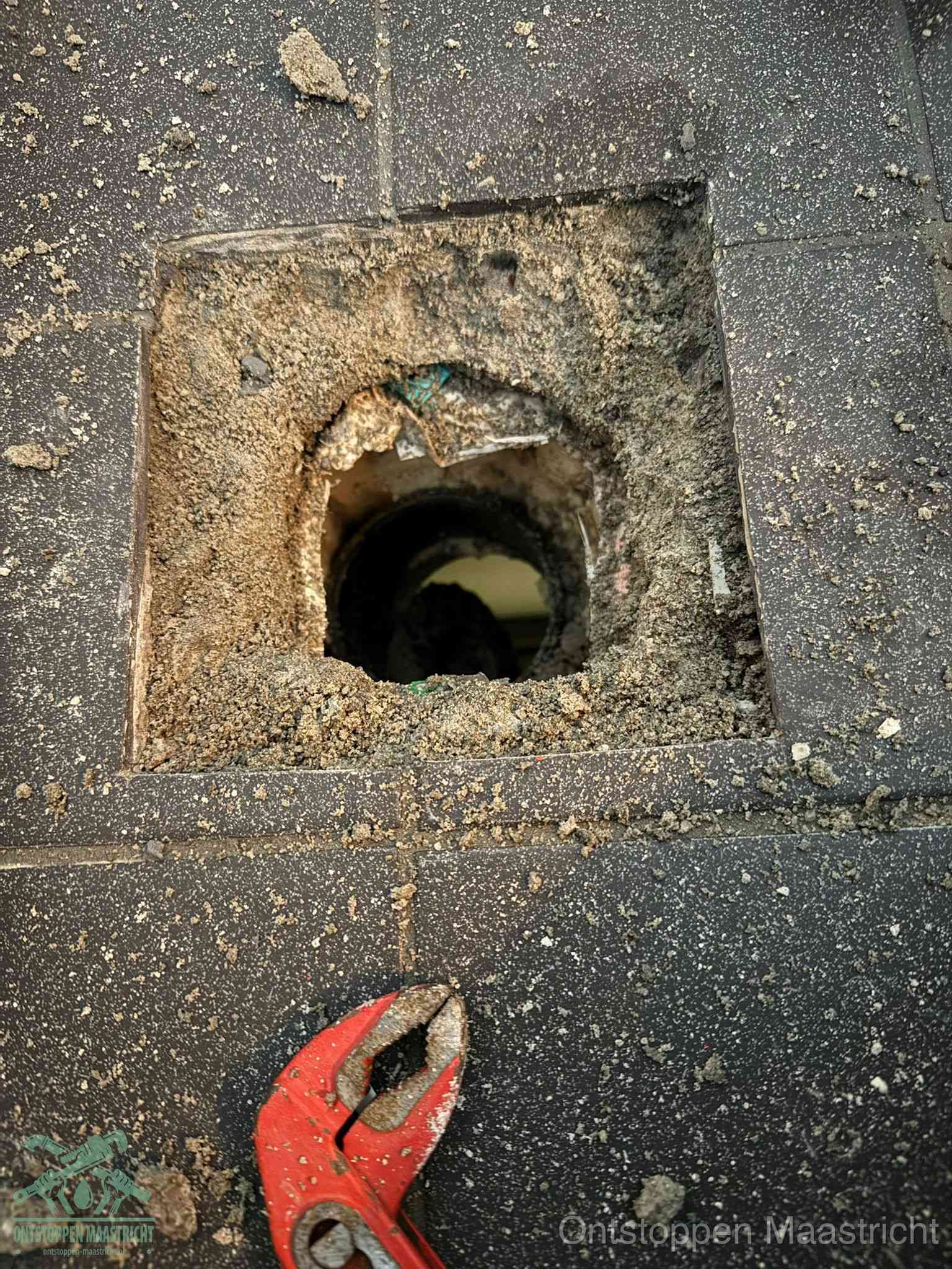 Een geopend rioolputje in een betontegelvloer met losgemaakt rooster en een zichtbare ronde afvoerbuis, het achterhalen waar de afvoerverstopping zit in Maastricht