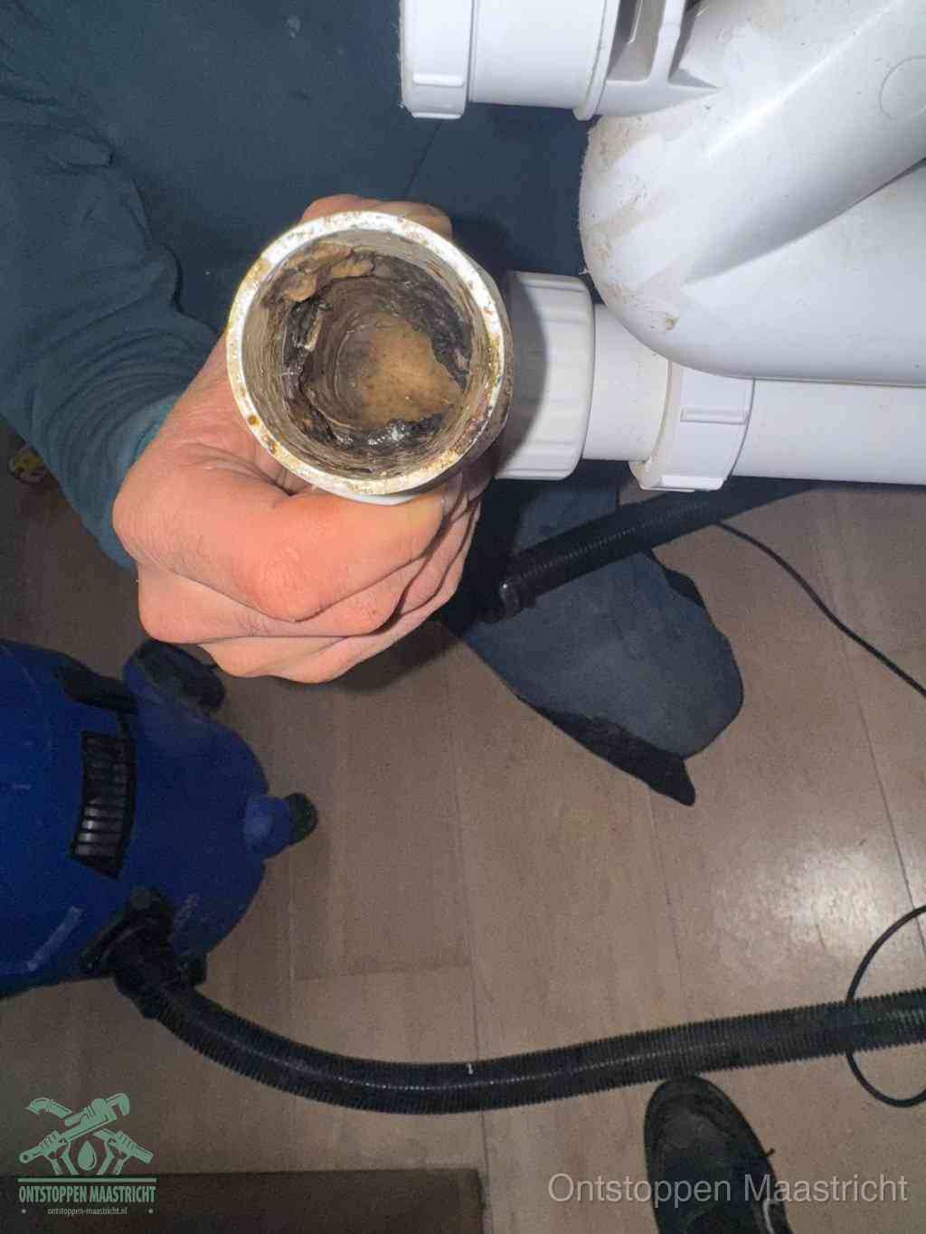 Een hand houdt een losgekoppeld PVC-afvoerbuisstuk vast dat van binnen volledig is dichtgeslibd met vet, vuil en aanslag, de meest voorkomende oorzaak van een verstopte afvoer in Maastricht