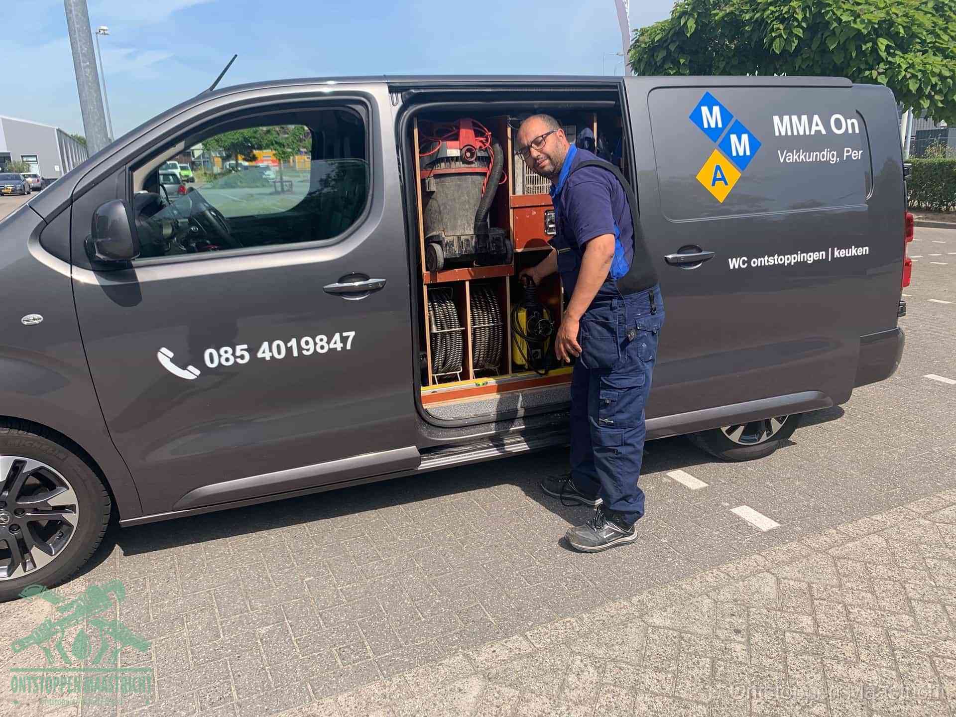 Een monteur bij de open schuifdeur van zijn bedrijfsbus op een parkeerplaats, klaar om de oorzaak van terugkerende afvoerverstoppingen aan te pakken in Maastricht