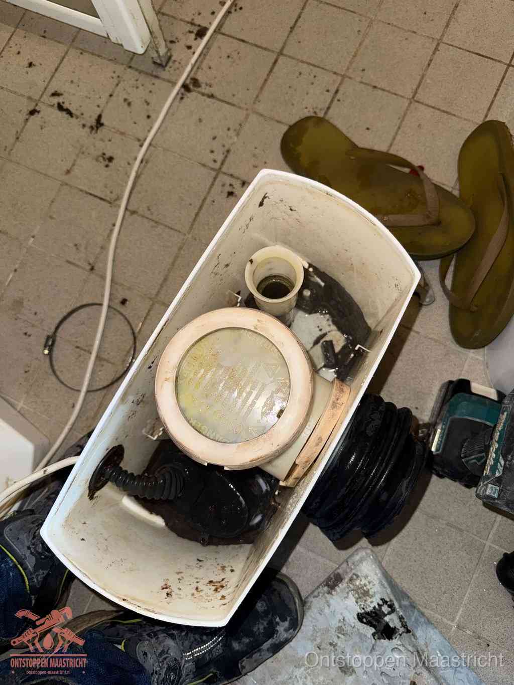 Een gedemonteerde toiletpot op de vloer met ontstoppingsveer en gereedschap ernaast, het verwijderen van een vastzittend voorwerp uit de wc in Maastricht
