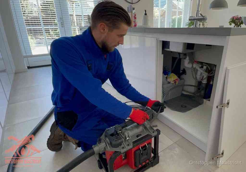 Een monteur voert een professionele elektrische ontstoppingsmachine in de afvoer onder de spoelbak tijdens het gootsteen ontstoppen in Maastricht